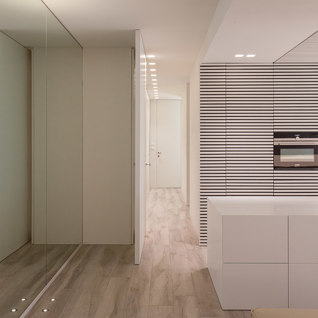 Minimalist interior with recessed ceiling lights illuminating a hallway, kitchen island, and wood-effect floor with mirrored wardrobe.