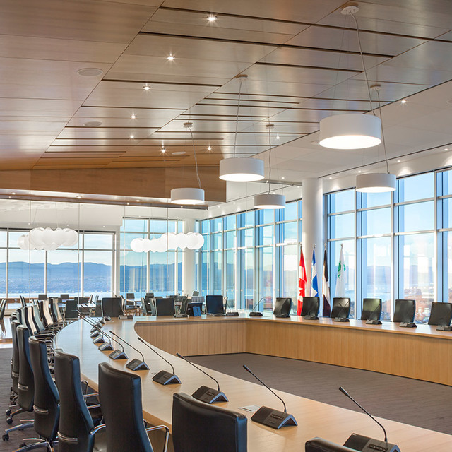 Modern council chamber with Artemide cylindrical pendant lights illuminating a curved conference table, floor-to-ceiling windows, wood ceiling.