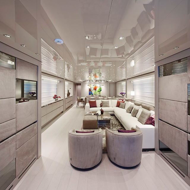 Luxury yacht interior with recessed ceiling lights, a large white sectional sofa, two round armchairs, and colorful pendant fixtures overhead