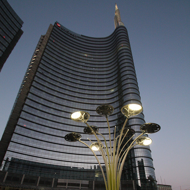 Artemide Pale outdoor lamps with golden stems and disc-shaped heads illuminate Unicredit Tower plaza in Milan at dusk