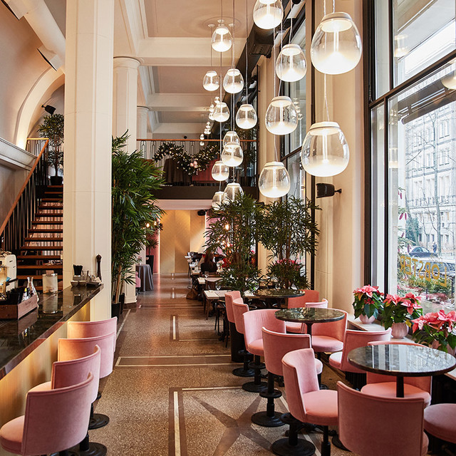 Elegant restaurant interior with cascading glass globe pendant lights illuminating pink velvet chairs, dark marble tables, and lush tropical plants.