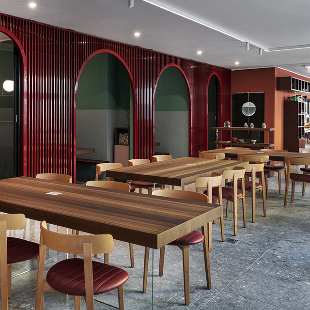 Modern restaurant interior with red arched dividers, wooden tables, chairs with burgundy seats, and recessed ceiling lighting.
