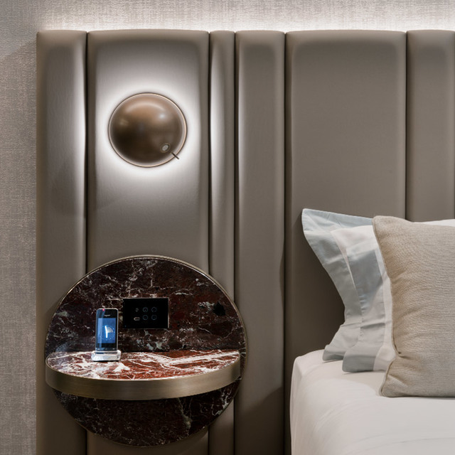 Artemide bronze sphere wall lamp with halo backlight mounted on padded headboard above a semicircular dark marble bedside table
