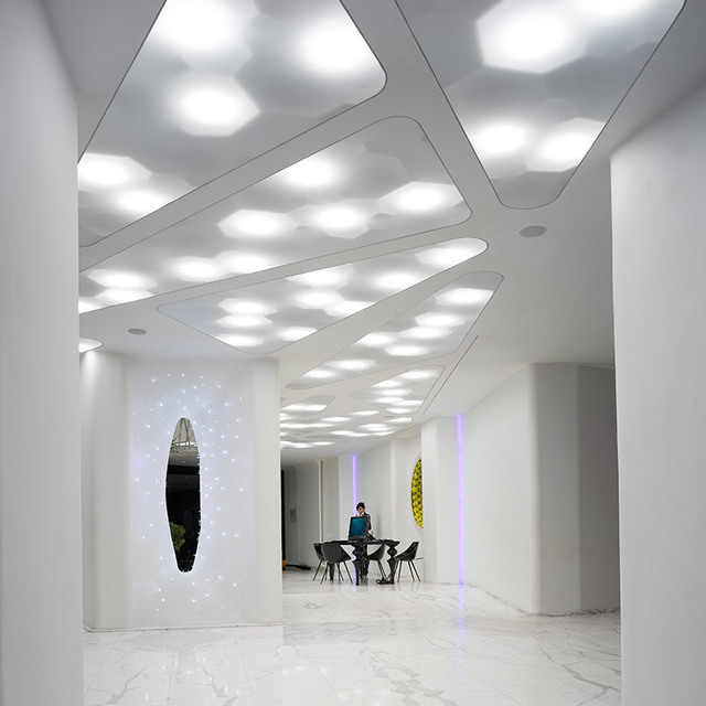 Modern white interior with organic-shaped ceiling panels featuring recessed lights, creating a luminous corridor with marble floor.
