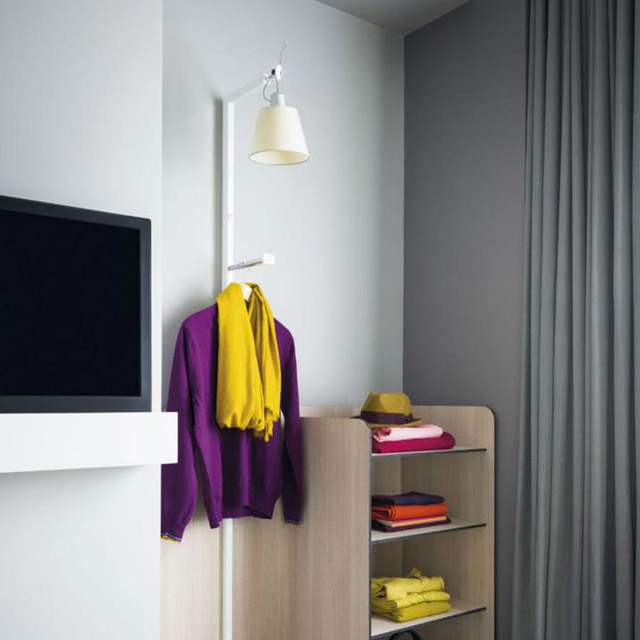 Artemide Tolomeo wall lamp with cream shade mounted in a wardrobe area with colorful folded clothes on wooden shelves