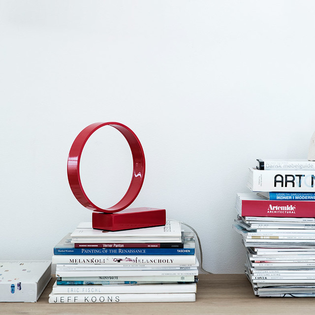 Artemide red circular LED table lamp with glossy ring design, displayed on a stack of art and design books