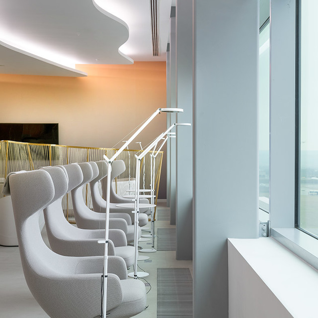 Lounge area with a row of grey pod chairs, each paired with a white Artemide Demetra floor lamp, near floor-to-ceiling windows.