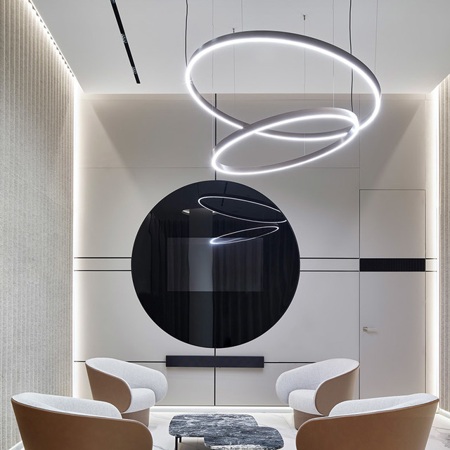 Modern lounge with overlapping circular LED pendant rings in black, suspended above seating area with large black circular wall art.