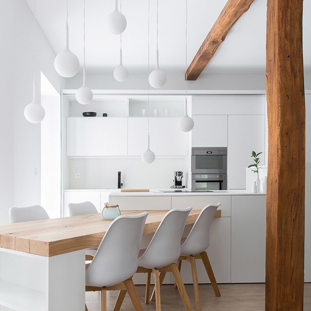 Modern white kitchen with wooden dining table, Scandinavian chairs, and multiple white spherical pendant lights hanging from ceiling