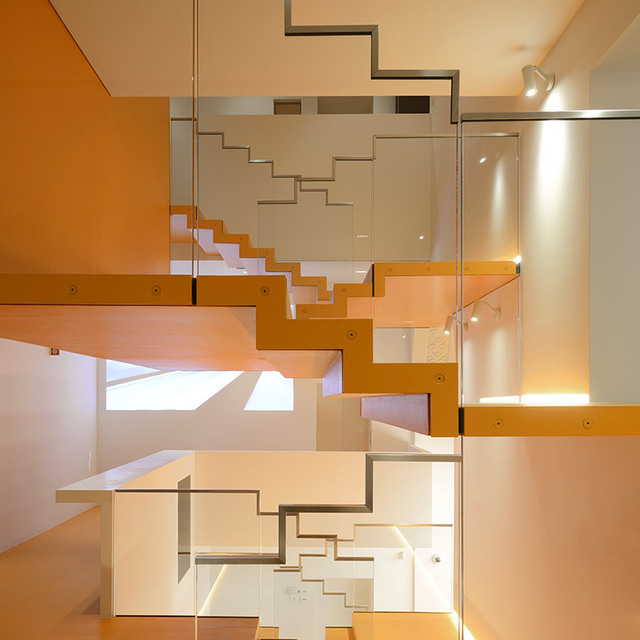 Multi-level interior staircase with orange and white geometric design, glass railings, and warm accent lighting on upper walls.