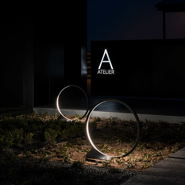 Two Artemide circular LED floor lamps with glowing ring shapes illuminate a garden at night in front of an Atelier building