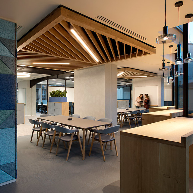 Modern office with wooden slatted ceiling, linear LED lights, pendant glass lamps over a bar counter, and a meeting table with chairs.