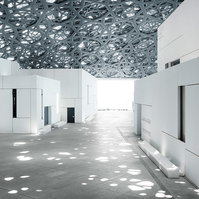 Louvre Abu Dhabi interior with iconic geometric dome casting dappled light patterns on white walls and grey stone floor