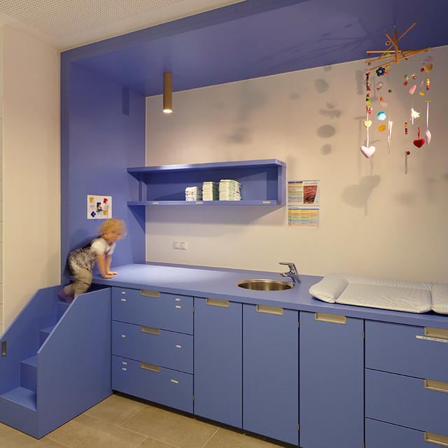 Children's room with blue cabinetry, a cylindrical pendant light illuminating a changing area with sink and colorful mobile above.