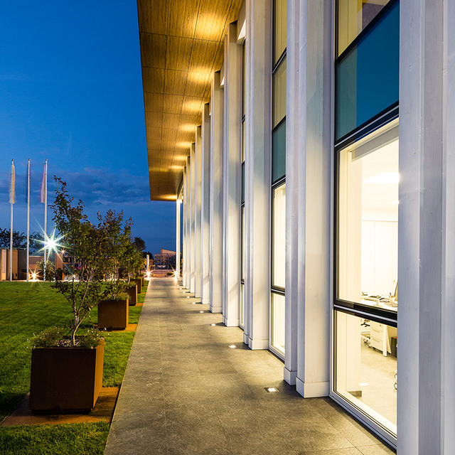 Modern building exterior at dusk with Artemide recessed floor uplights illuminating white columns along a glass facade walkway.