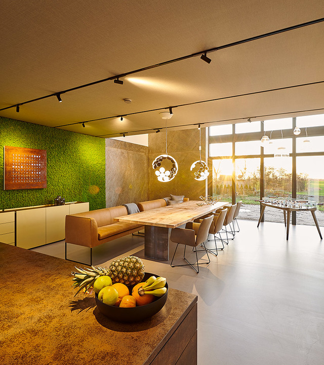 Modern open-plan dining area with Artemide pendant lights above a long table, track lighting, green moss wall, and floor-to-ceiling windows