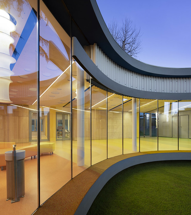 Curved glass facade of a modern building at dusk, interior illuminated by Artemide linear LED ceiling lights creating warm ambient lighting.