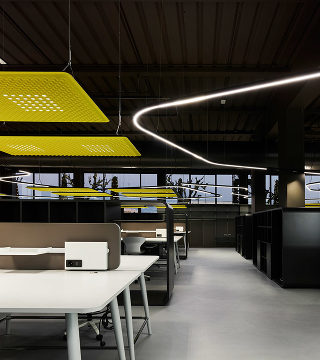 Modern office with Artemide curved linear pendant light and yellow perforated acoustic pendant panels above white workstations