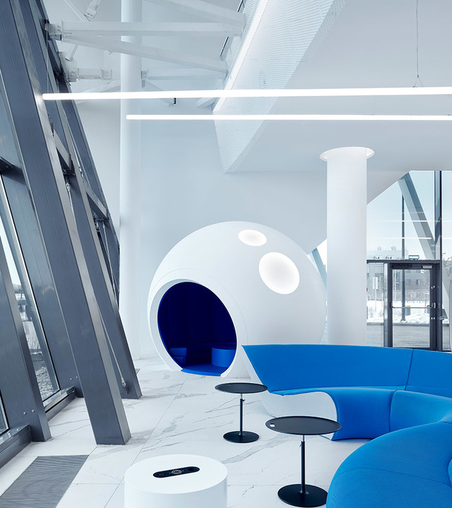 Modern office lounge with Artemide linear ceiling lights, a white spherical pod seating area, and vibrant blue modular sofas on marble floor