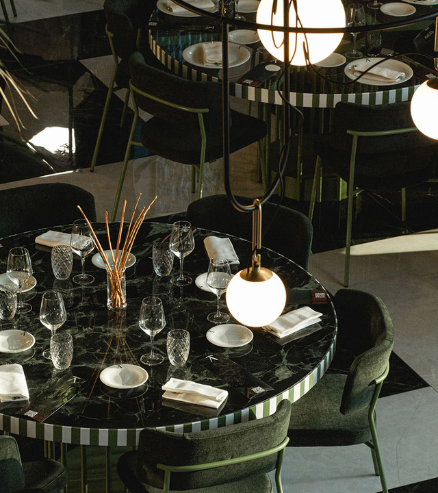 Elegant restaurant dining room with marble tables set for dinner, featuring spherical white glass pendant and table lamps with brass details.