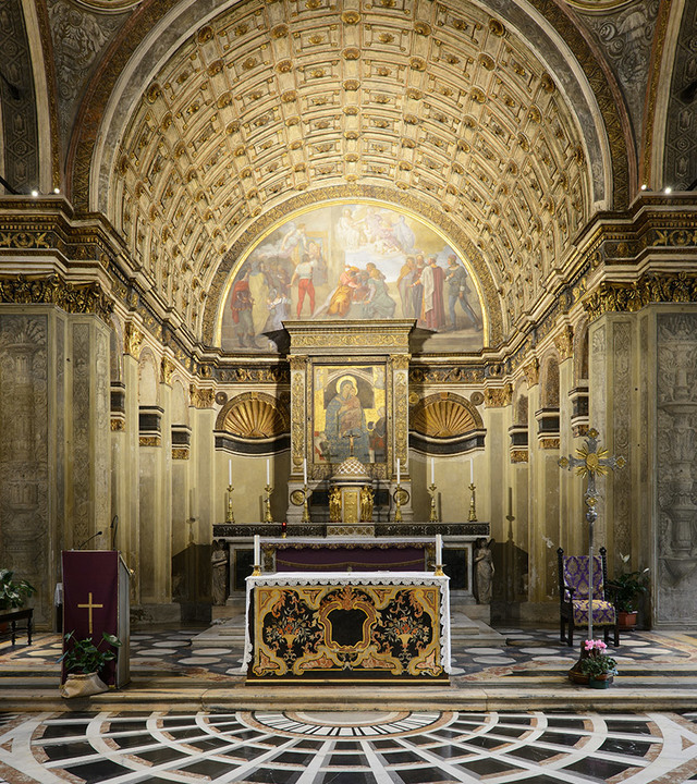 Ornate church apse with gilded barrel vault, Renaissance frescoes, decorated altar, and marble inlaid floor bathed in warm light