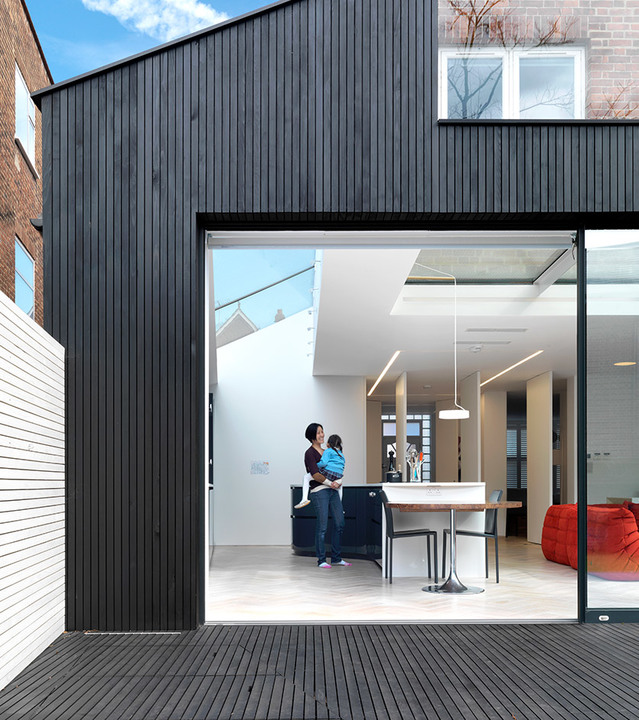 Modern open-plan interior with Artemide recessed linear ceiling lights and pendant lamp over dining table, viewed through large glass sliding doors.