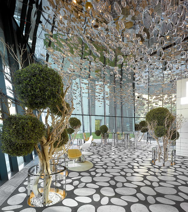 Luxurious lobby with sculptural glass bubble ceiling installation, manicured topiary trees, pebble-patterned floor, and modern seating.