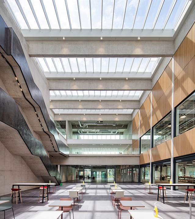 Modern atrium with skylights, recessed ceiling lights, wood-paneled walls, and open seating area on polished concrete floor