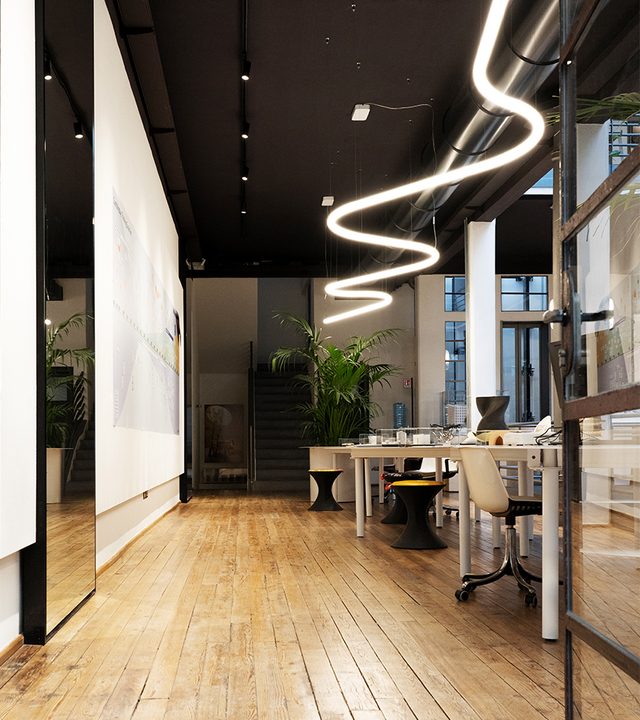Artemide Alphabet of Light pendant lamp in a sinuous wave shape illuminates a modern office with wooden floors and dark ceiling.