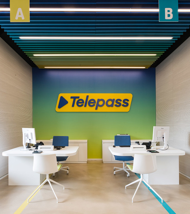 Telepass office with two workstations under Artemide linear ceiling lights on a colorful teal and yellow slatted ceiling.