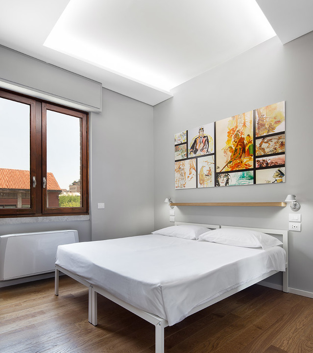 Modern bedroom with white bed, colorful wall art, and Artemide wall reading lights on headboard shelf, lit ceiling recess above