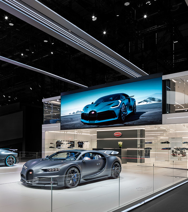 Bugatti showroom with a dark grey supercar on display, illuminated by Artemide linear ceiling lights and recessed spotlights.