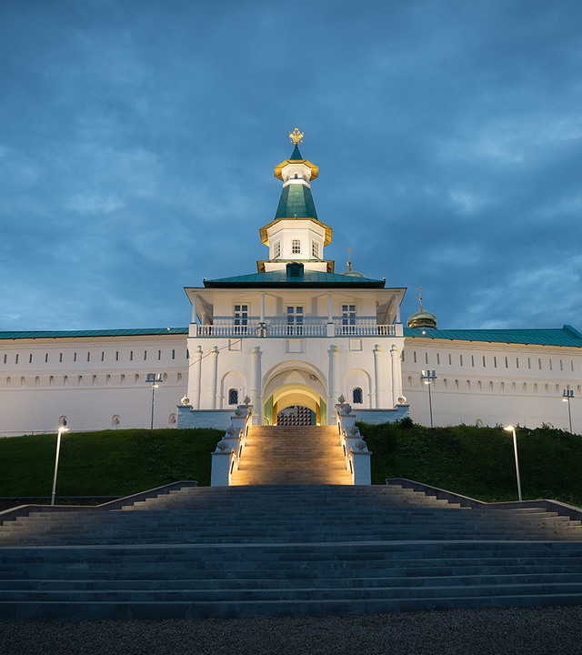 Artemide lighting illuminates the grand staircase and entrance gate of a white Orthodox monastery at dusk, with a golden-topped tower.