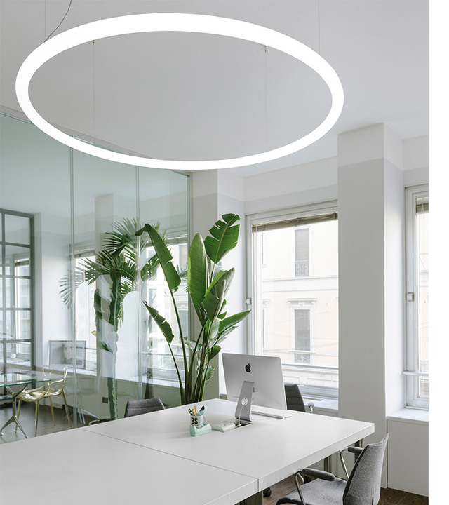Artemide circular LED pendant light illuminating a modern white office workspace with desk, iMac, and tropical plants.