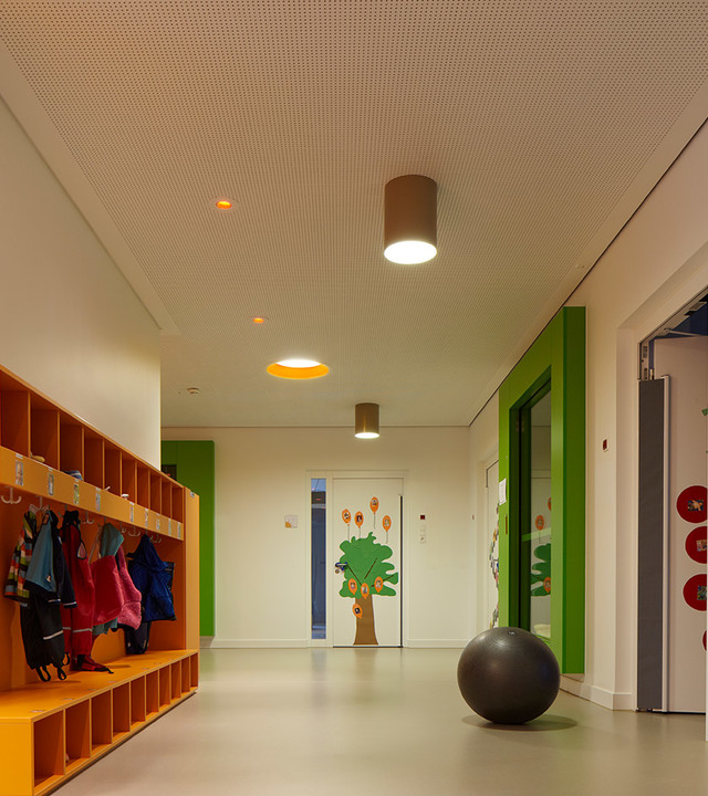 School corridor with Artemide cylindrical ceiling lights illuminating colorful cubbies, green walls, and a playful tree mural.