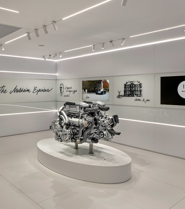 Luxury showroom with Artemide recessed linear and track lighting illuminating a car engine displayed on a white pedestal
