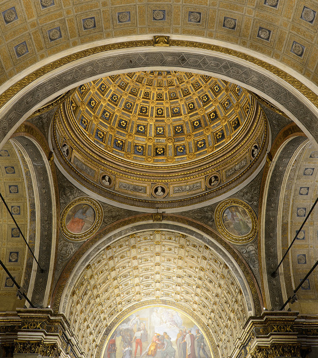 Interior view of a Renaissance church dome with gilded coffered ceiling, ornate arches, and classical frescoes below.