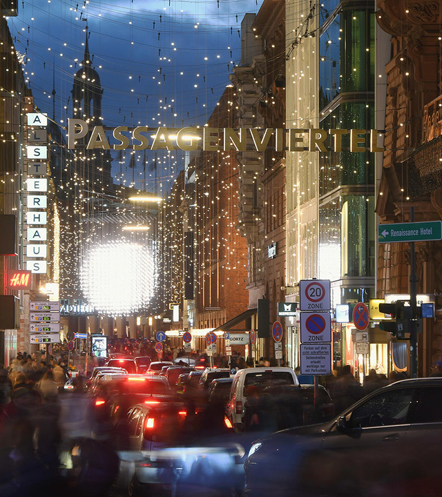 Passagenviertel shopping street at dusk, adorned with festive string lights and a glowing sign above busy traffic.