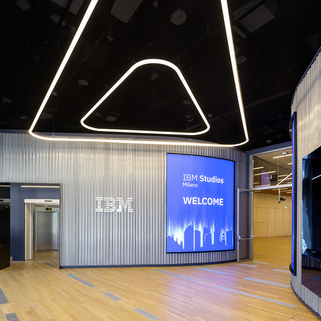 IBM Studios Milano entrance with Artemide triangular LED linear pendant lights on black ceiling above wooden floor.