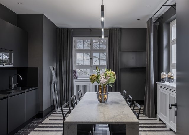 Dark dining room with marble table, black chairs, and a sleek pendant light above, geometric floor, floral centerpiece.
