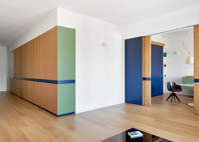 Modern interior with wood and colorful blue-green cabinetry, open doorway revealing a workspace with a pendant lamp and task lamp.