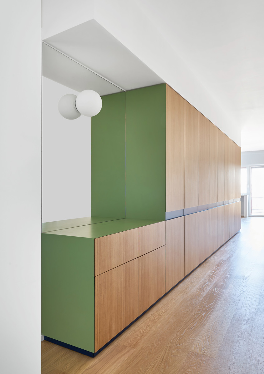 Artemide spherical white wall lamp mounted on white wall beside green and wood built-in cabinetry in modern interior