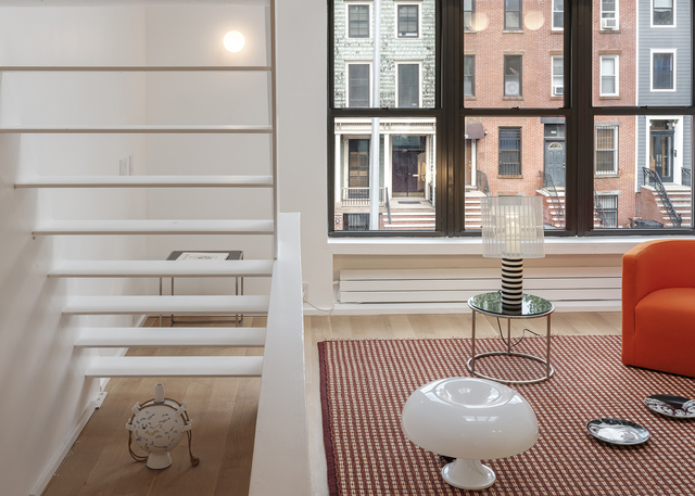 Modern living room with Artemide table lamp and white globe floor lamp near large windows overlooking urban brownstone buildings