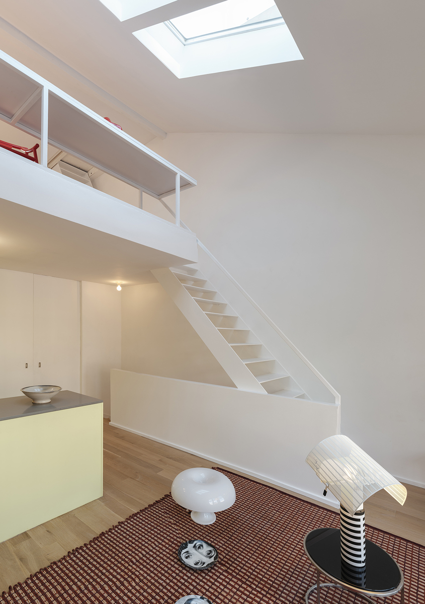 Modern duplex interior with Artemide Nesso table lamp and Chiara floor lamp on a patterned rug, white staircase and skylight above
