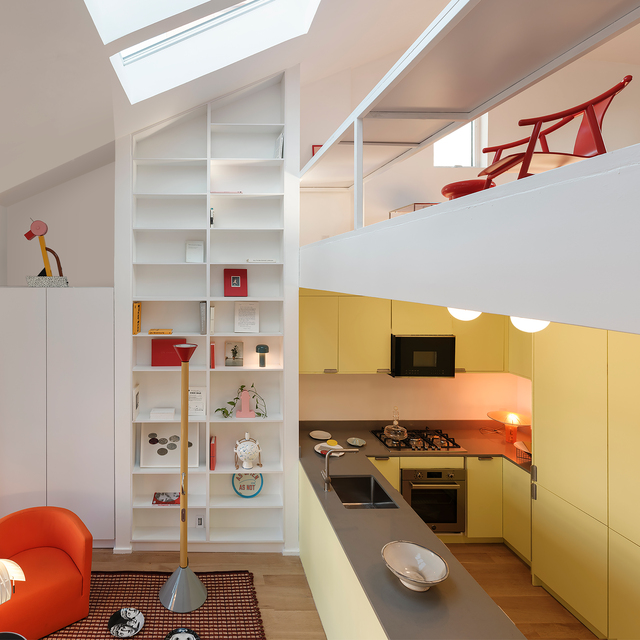 Modern loft kitchen with yellow cabinets, skylight, white bookshelf, and Artemide floor lamp with grey base in living area