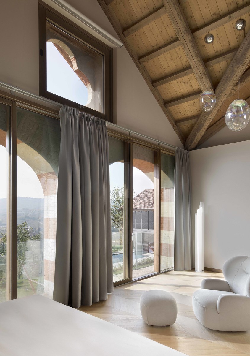 Bright room with vaulted wooden ceiling, large windows, grey curtains, white rounded chairs, and two transparent glass bubble pendant lamps