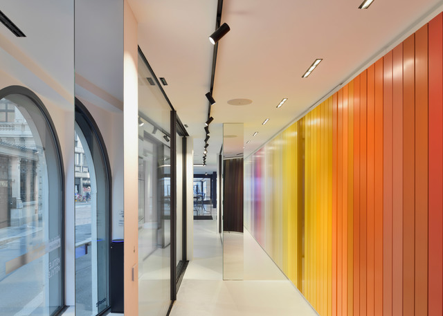 Modern corridor with black Artemide track spotlights on ceiling, illuminating a vibrant gradient wall in yellow, orange, and red tones.