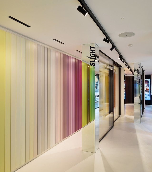 Artemide showroom corridor with track lighting on black rails illuminating a colorful striped wall display and mirrored columns