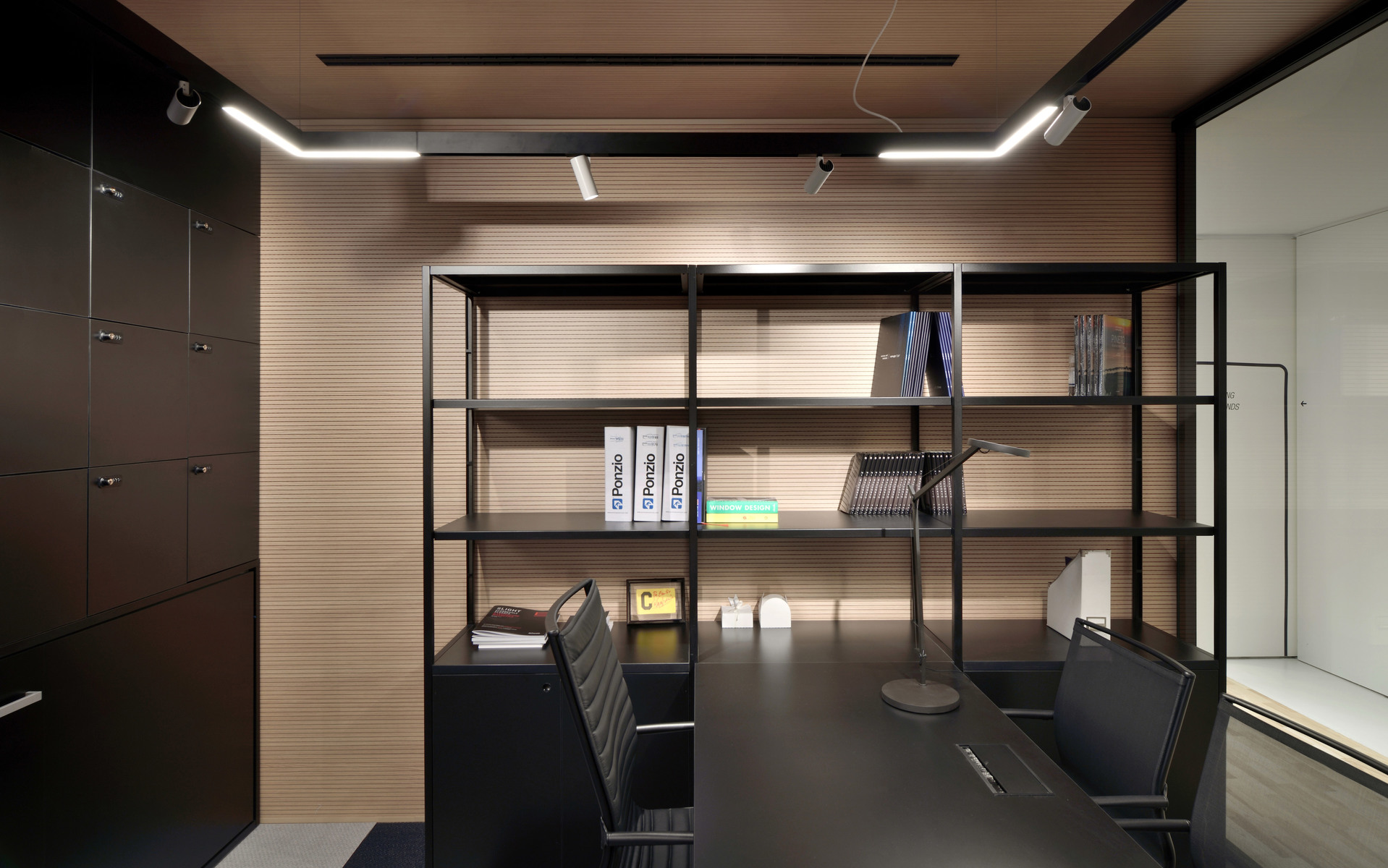 Modern office with dark desk, open shelving unit, and two slim linear LED ceiling lights illuminating the workspace.