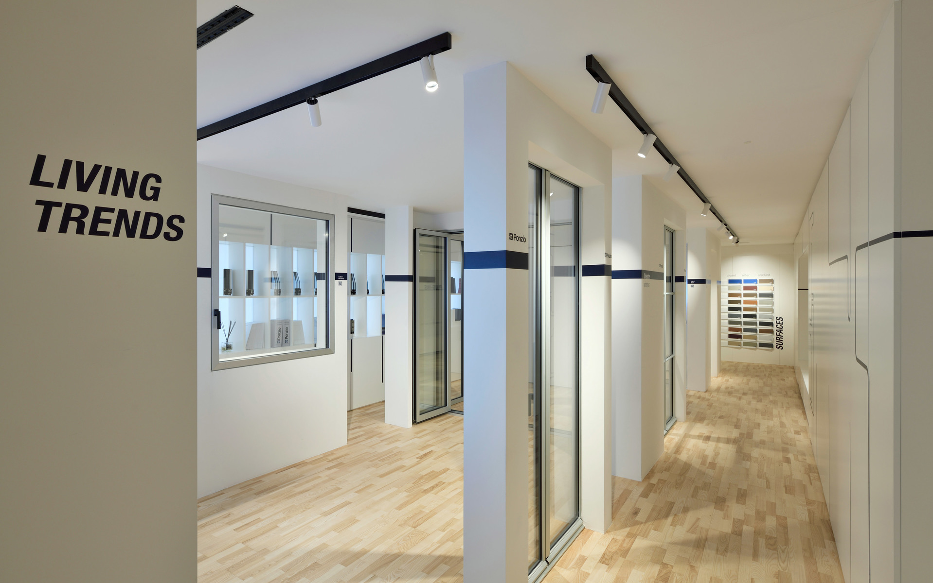 Modern showroom corridor labeled 'Living Trends' with black track lighting on white ceiling and light wood flooring.
